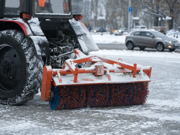 Tractor brushes snow on the road in the evening